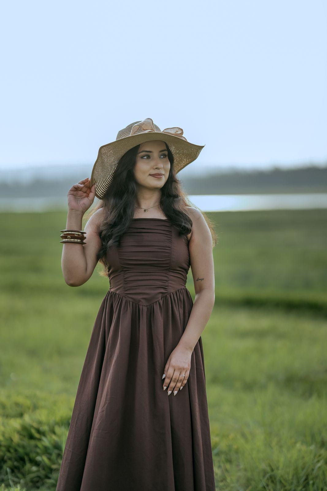 Apeksha in a brown dress and sun hat in the field